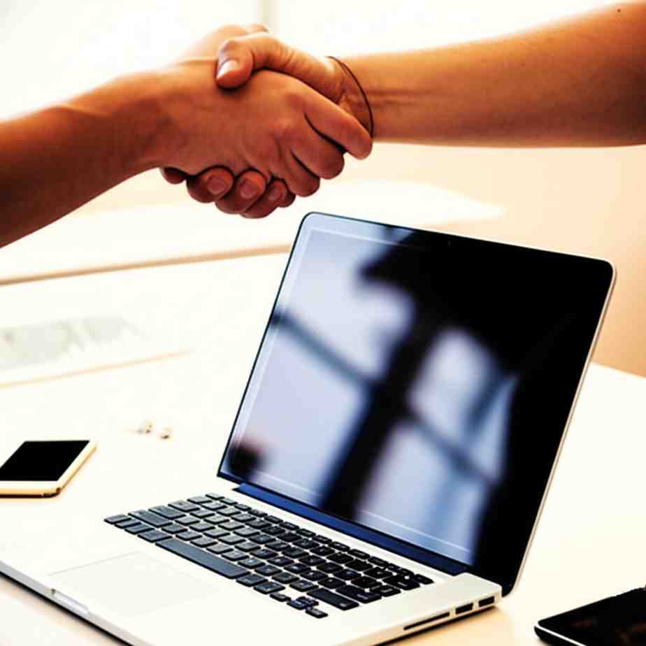 About Us Two people shaking hands over a laptop or brainstorming with tech gear around—a visual metaphor for collaboration